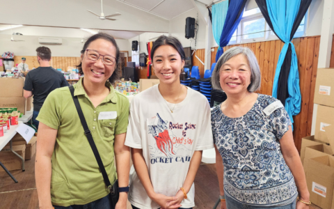 Three women smiling in room with boxes behind them.