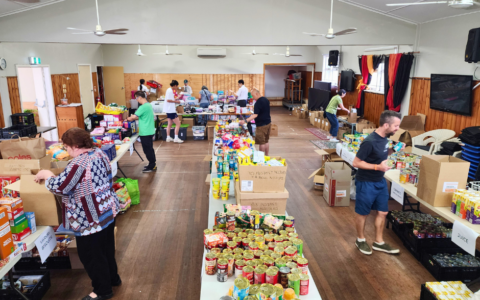 A room with tables holding groups of food items. People are placing items on tables.