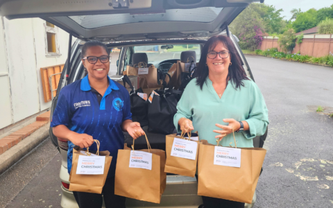 Two woman smiling in front of car boot with gift bags.