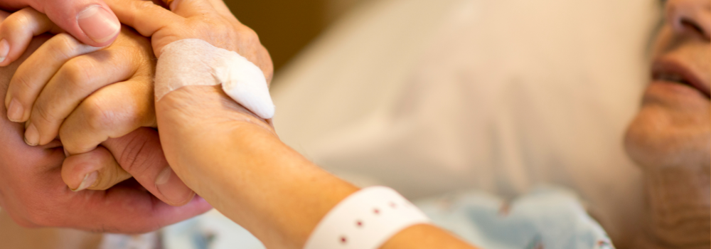 An elderly woman in a hospital bed holding someone's hands